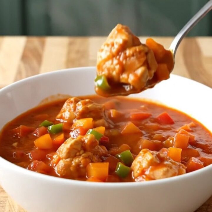 A close-up of chicken sauce piquante in a white bowl with steam rising, showing tender chicken and colorful peppers.