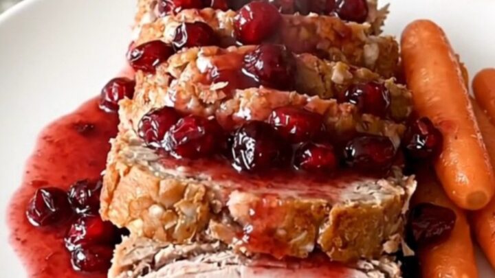 A perfectly cooked turkey meatloaf in a black slow cooker, topped with cranberry sauce and surrounded by baby carrots.