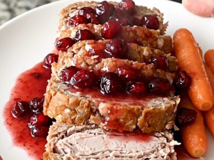 A perfectly cooked turkey meatloaf in a black slow cooker, topped with cranberry sauce and surrounded by baby carrots.