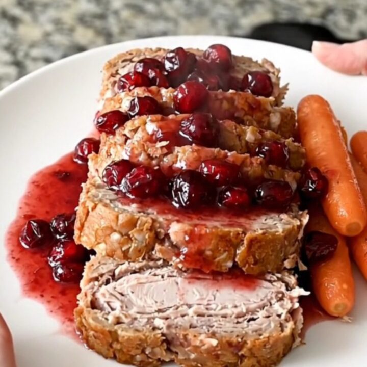 A perfectly cooked turkey meatloaf in a black slow cooker, topped with cranberry sauce and surrounded by baby carrots.