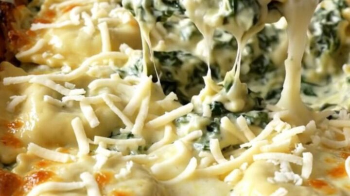 A rectangular ceramic dish filled with baked cheese ravioli covered in creamy spinach alfredo sauce and golden melted