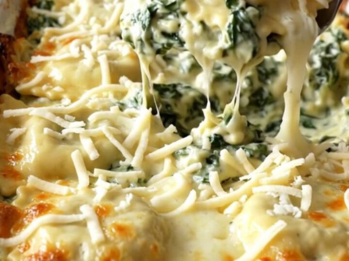 A rectangular ceramic dish filled with baked cheese ravioli covered in creamy spinach alfredo sauce and golden melted