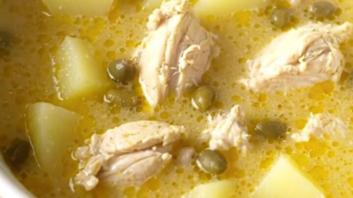 A bowl of creamy chicken piccata soup topped with fresh parsley and capers on a beige kitchen counter.
