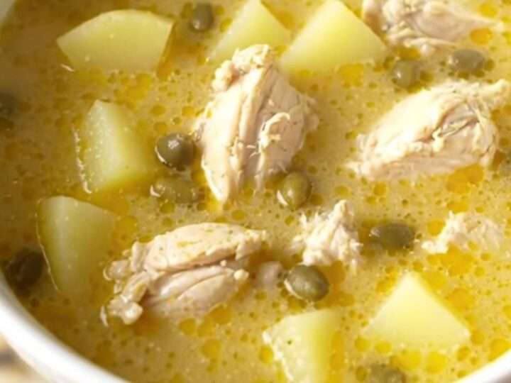 A bowl of creamy chicken piccata soup topped with fresh parsley and capers on a beige kitchen counter.