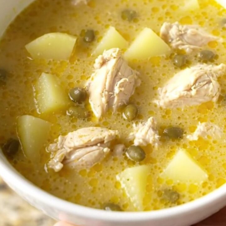 A bowl of creamy chicken piccata soup topped with fresh parsley and capers on a beige kitchen counter.