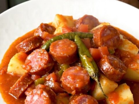 A close-up shot of the finished smoked sausage and potato dish in a white bowl with a rich tomato sauce.