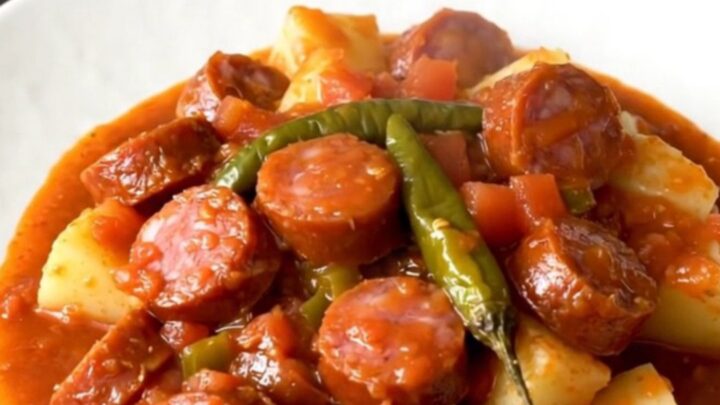 A close-up shot of the finished smoked sausage and potato dish in a white bowl with a rich tomato sauce.