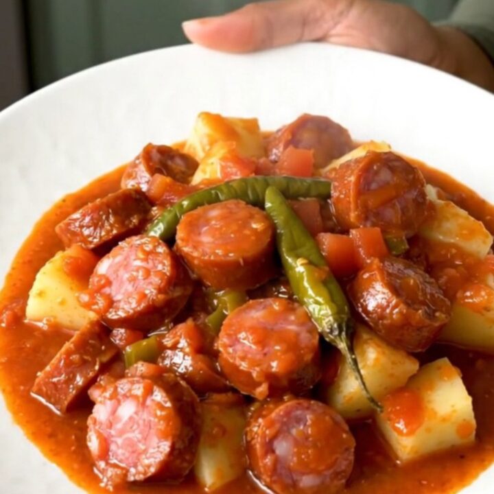 A close-up shot of the finished smoked sausage and potato dish in a white bowl with a rich tomato sauce.