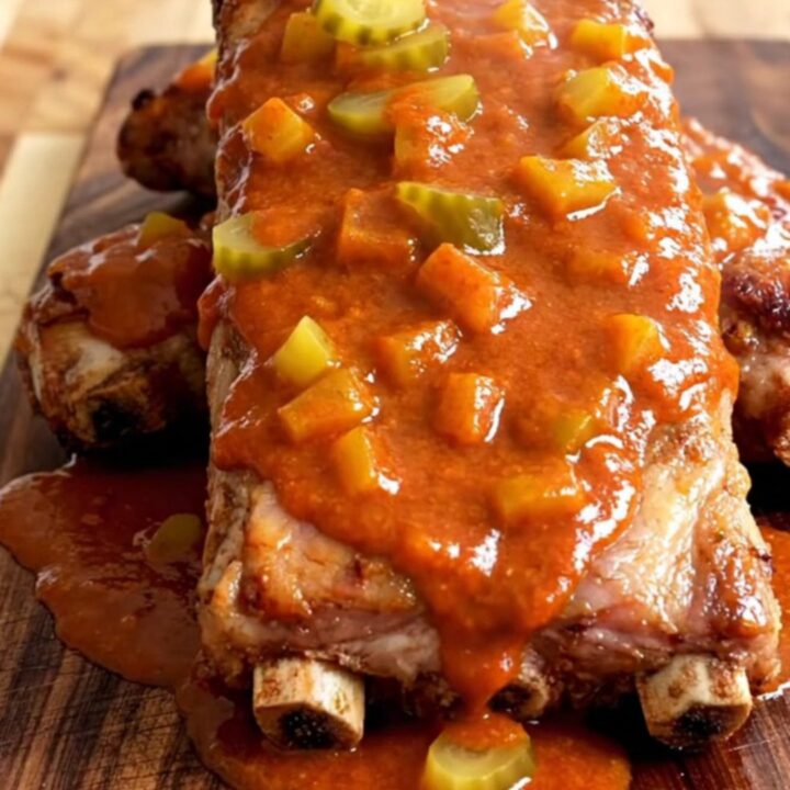 A close-up of Nashville hot country-style ribs served on a wooden board with a thick, spicy butter sauce.