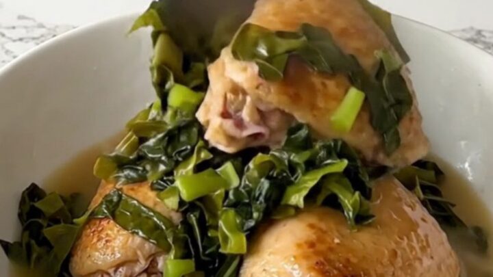 A top-down view of raw chicken thighs and chopped collard greens in a black slow cooker insert.