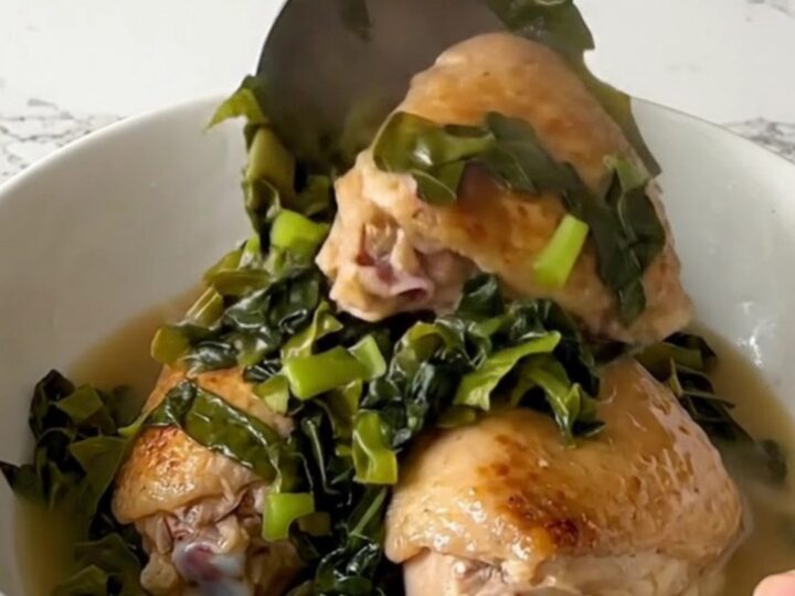 A top-down view of raw chicken thighs and chopped collard greens in a black slow cooker insert.