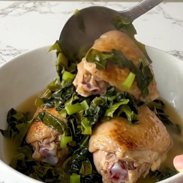 A top-down view of raw chicken thighs and chopped collard greens in a black slow cooker insert.