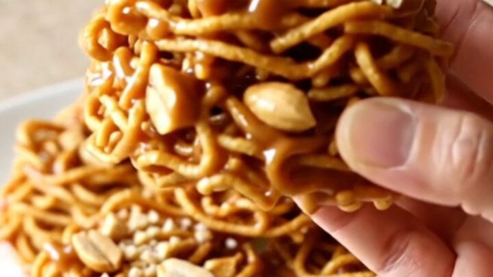 A close-up of golden, crunchy butterscotch haystacks piled on a white plate with a soft-focus kitchen background.