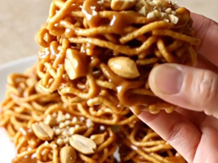 A close-up of golden, crunchy butterscotch haystacks piled on a white plate with a soft-focus kitchen background.