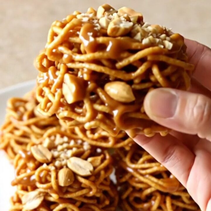 A close-up of golden, crunchy butterscotch haystacks piled on a white plate with a soft-focus kitchen background.