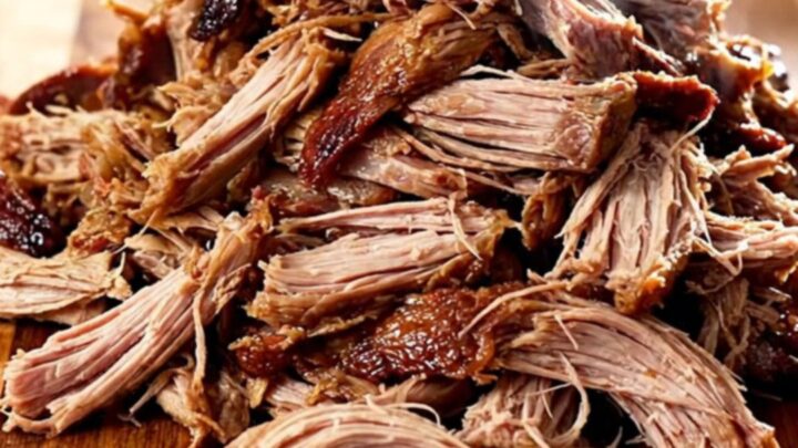 A close-up view of tender, shredded Kalua pork piled high on a wooden board, showing natural steam.