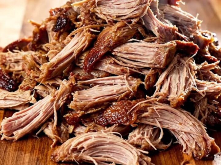 A close-up view of tender, shredded Kalua pork piled high on a wooden board, showing natural steam.