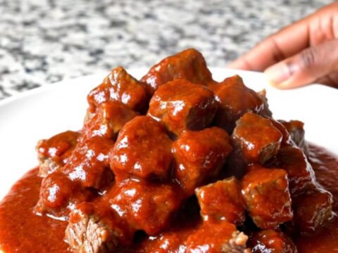 A close-up of tender beef tips in a thick, glossy red gochujang sauce served in a slow cooker insert.