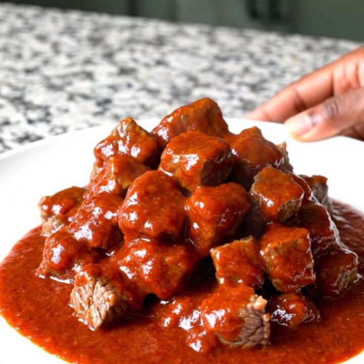 A close-up of tender beef tips in a thick, glossy red gochujang sauce served in a slow cooker insert.
