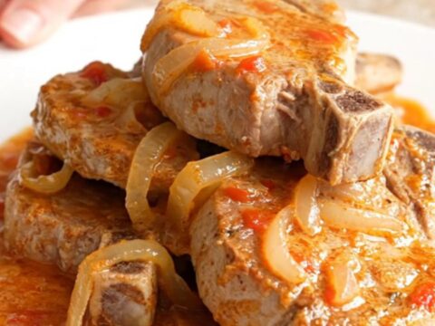 A close-up of tender, braised pork chops covered in a rich, creamy tomato basil sauce on a white plate.