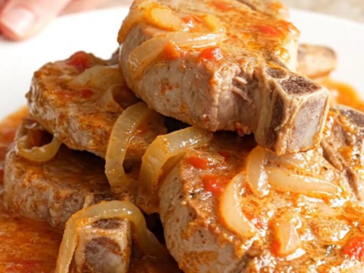 A close-up of tender, braised pork chops covered in a rich, creamy tomato basil sauce on a white plate.