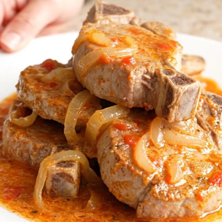 A close-up of tender, braised pork chops covered in a rich, creamy tomato basil sauce on a white plate.