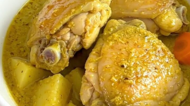 A top-down view of a black slow cooker filled with bone-in chicken thighs, potato cubes