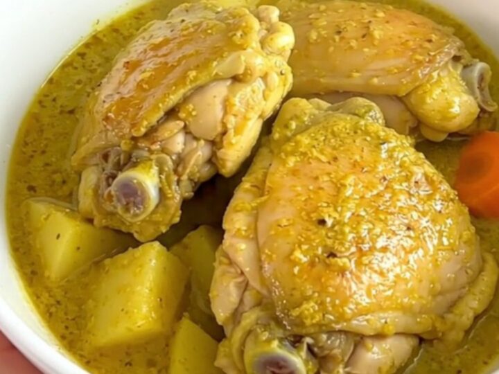 A top-down view of a black slow cooker filled with bone-in chicken thighs, potato cubes
