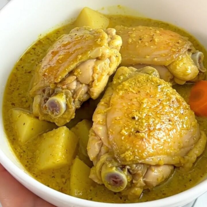 A top-down view of a black slow cooker filled with bone-in chicken thighs, potato cubes
