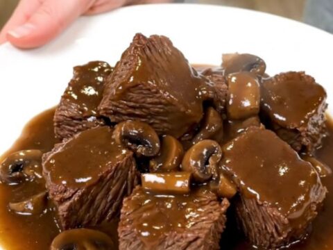 A rustic slow cooker filled with tender beef cubes and mushrooms in a rich Marsala sauce.