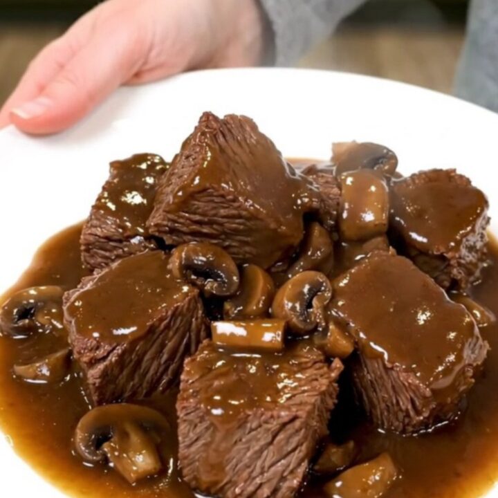 A rustic slow cooker filled with tender beef cubes and mushrooms in a rich Marsala sauce.