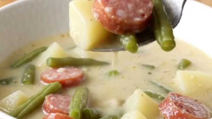 A steaming bowl of creamy smoked sausage, green bean, and potato soup on a rustic kitchen counter.