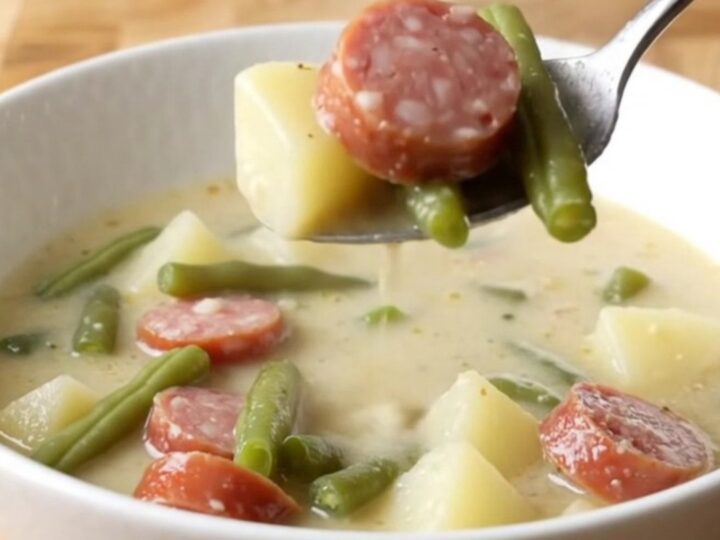 A steaming bowl of creamy smoked sausage, green bean, and potato soup on a rustic kitchen counter.