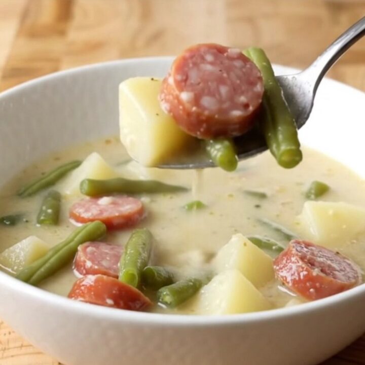 A steaming bowl of creamy smoked sausage, green bean, and potato soup on a rustic kitchen counter.