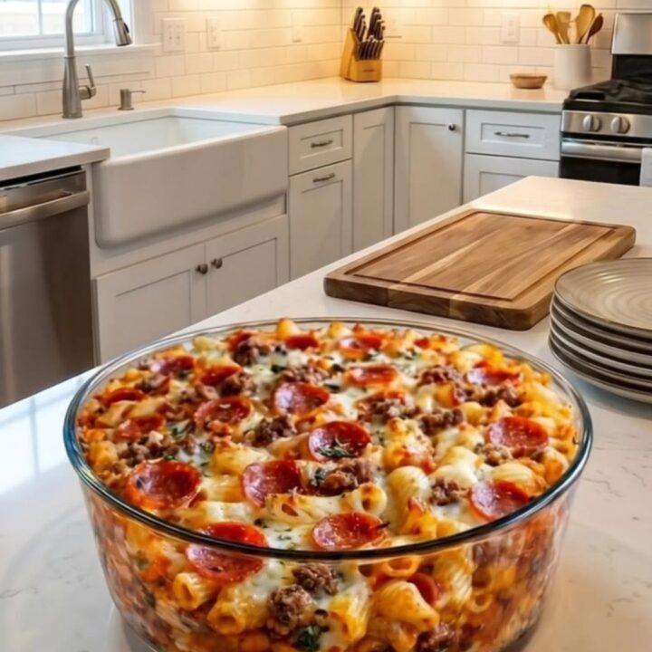 A close-up of a spoon lifting a portion of cheesy rigatoni pasta with pepperoni from a baking dish.