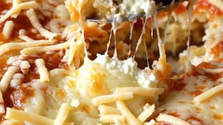 A large rectangular ceramic dish filled with unbaked pasta shells, dollops of ricotta, and marinara sauce.