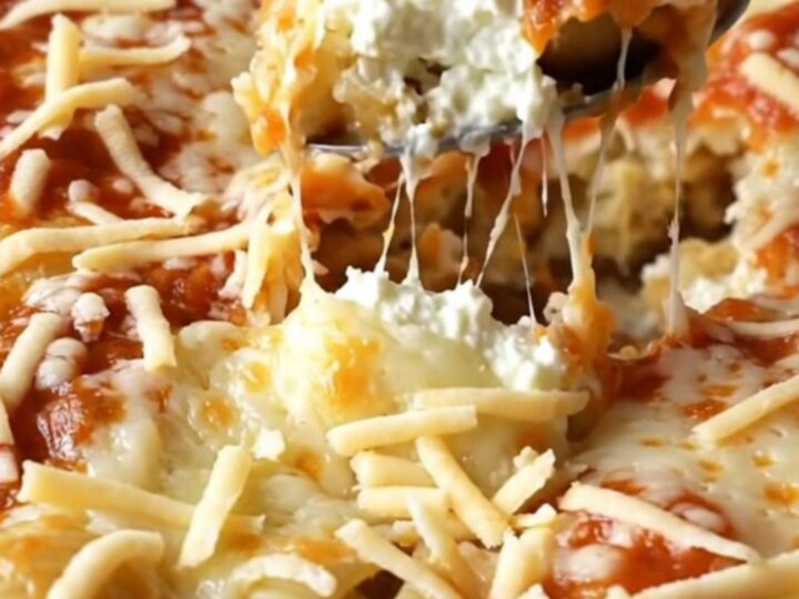 A large rectangular ceramic dish filled with unbaked pasta shells, dollops of ricotta, and marinara sauce.