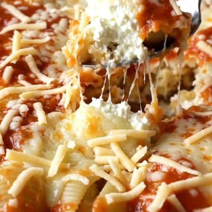 A large rectangular ceramic dish filled with unbaked pasta shells, dollops of ricotta, and marinara sauce.