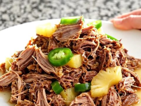 A slow cooker filled with tender pulled pork, pineapple chunks, and sliced jalapenos in a savory, aromatic juice.