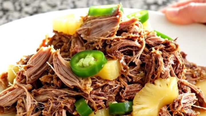 A slow cooker filled with tender pulled pork, pineapple chunks, and sliced jalapenos in a savory, aromatic juice.