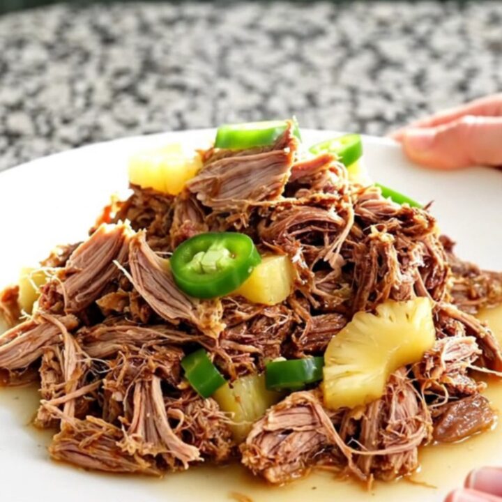 A slow cooker filled with tender pulled pork, pineapple chunks, and sliced jalapenos in a savory, aromatic juice.