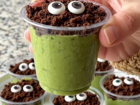 A tray of green pistachio pudding cups topped with cookie crumbs and candy eyes.