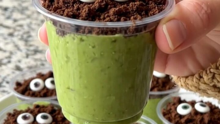 A tray of green pistachio pudding cups topped with cookie crumbs and candy eyes.