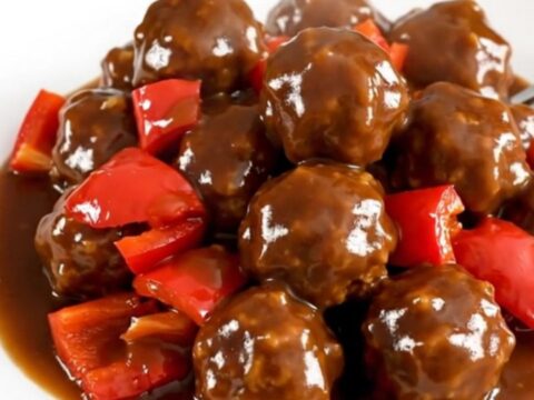 A slow cooker filled with turkey meatballs coated in a vibrant, glossy jerk sauce and diced red peppers.