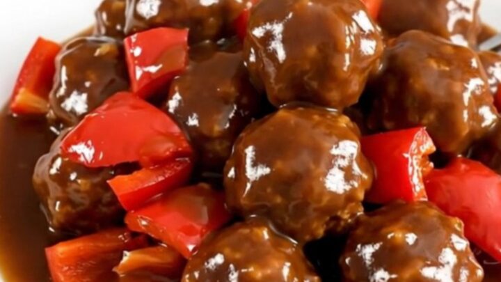 A slow cooker filled with turkey meatballs coated in a vibrant, glossy jerk sauce and diced red peppers.