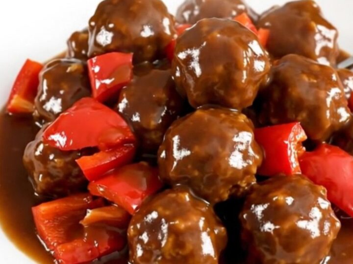 A slow cooker filled with turkey meatballs coated in a vibrant, glossy jerk sauce and diced red peppers.