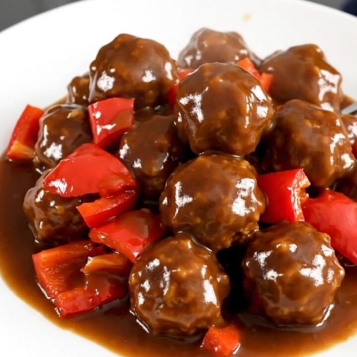 A slow cooker filled with turkey meatballs coated in a vibrant, glossy jerk sauce and diced red peppers.