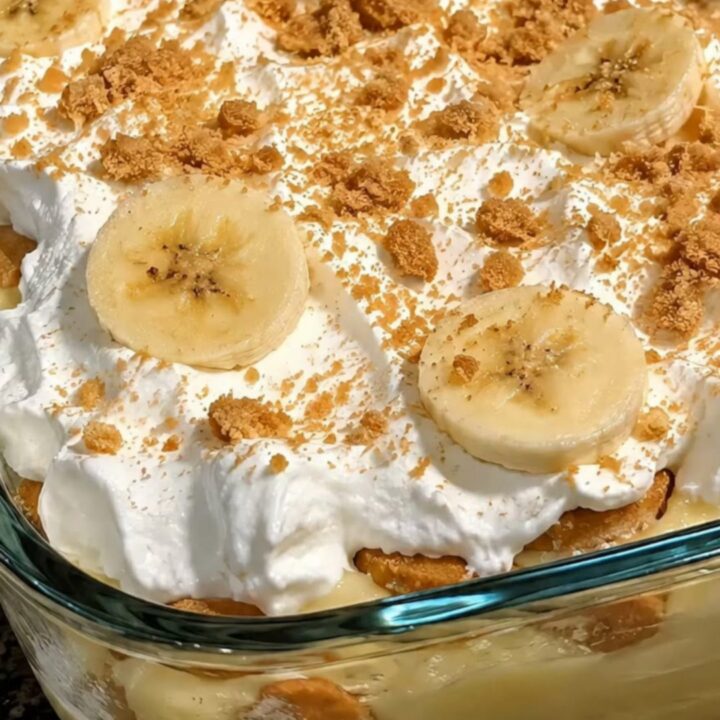 A large spoon scooping into a glass baking dish filled with layers of creamy vanilla pudding, banana slices, and wafers.