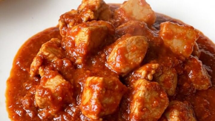 A vibrant bowl of slow-cooked chicken vindaloo with tender potatoes and a rich, spicy red sauce.