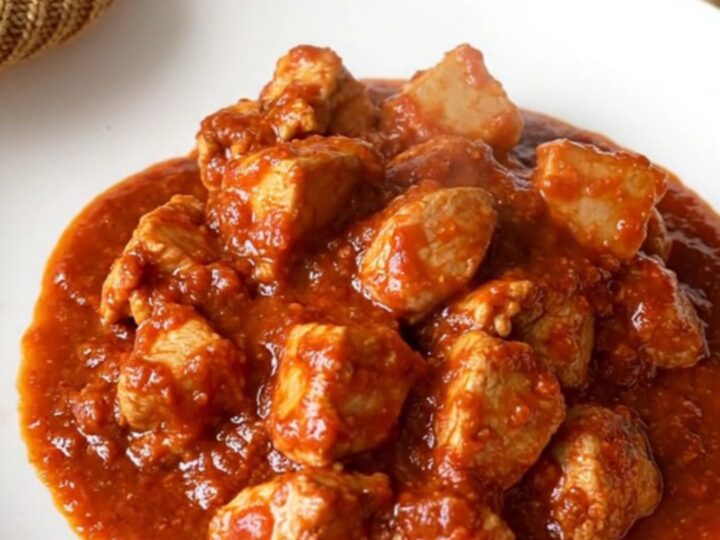 A vibrant bowl of slow-cooked chicken vindaloo with tender potatoes and a rich, spicy red sauce.